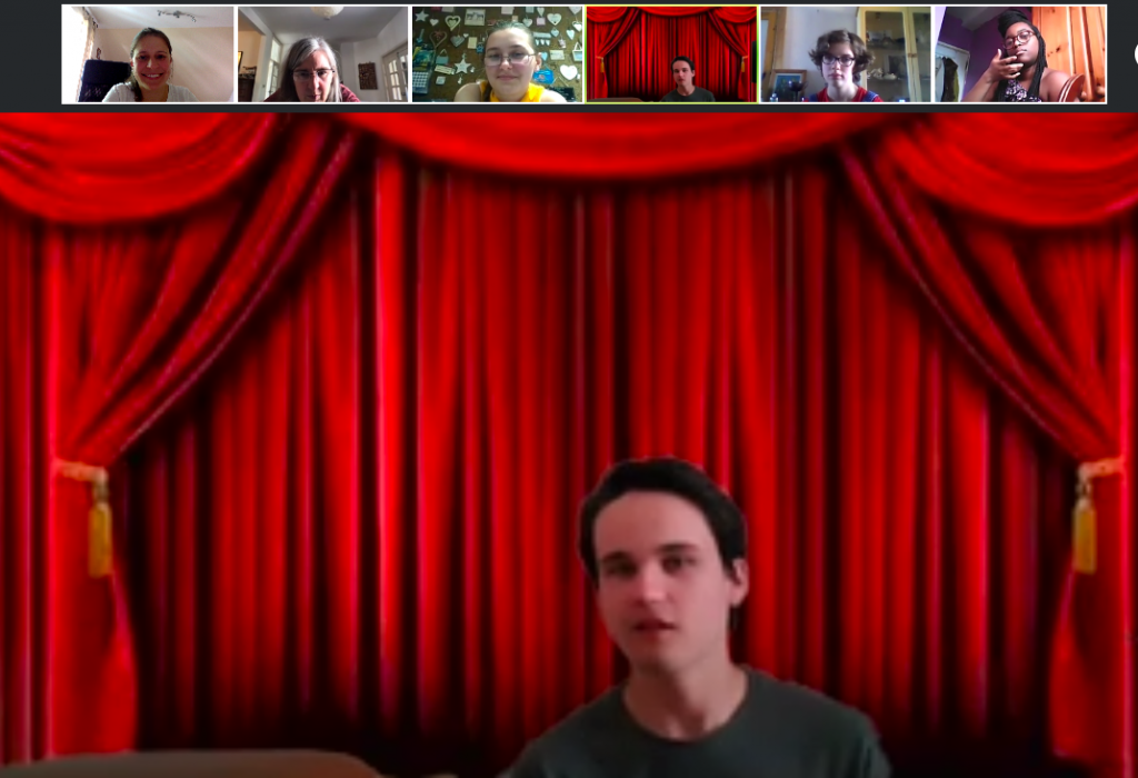 Cameron looks to camera against a Zoom background of red stage curtains with small images of other participants above